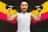 A man holds dumbbells in his hands raised up to head height for a story about weight lifting health benefits.