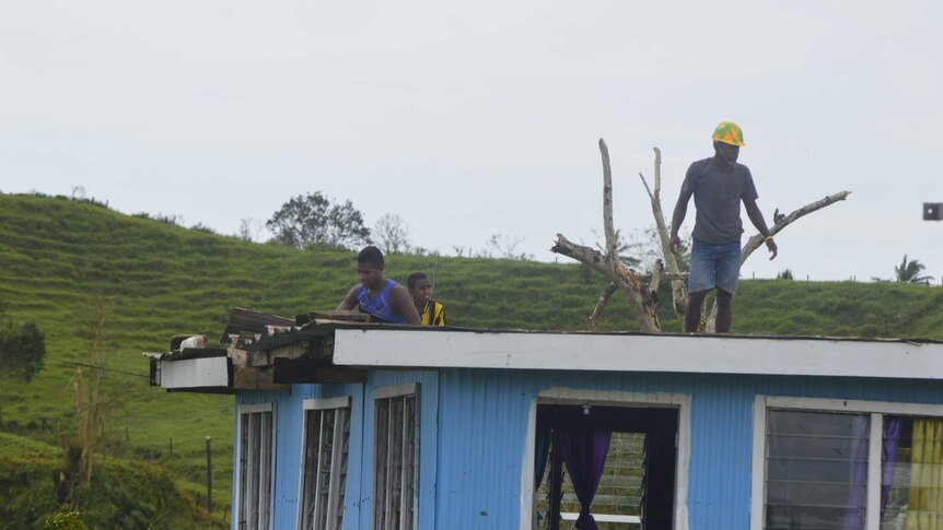 A man stands on the roof of a damaged house in Fiji