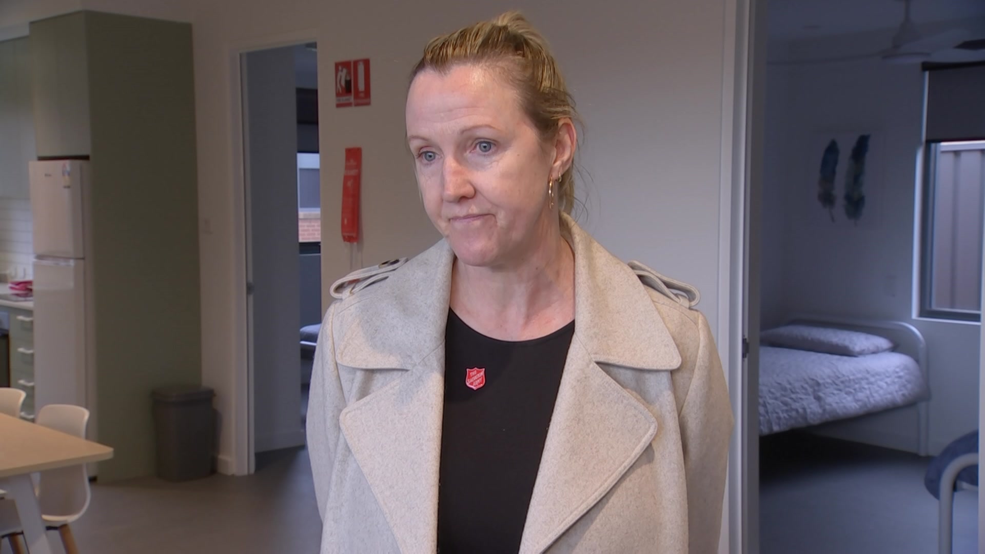 A woman standing with a beige jacket and looking serious 