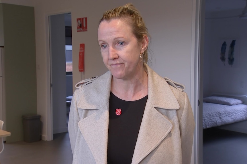 A woman stanidng with a beige jacket and looking serious 