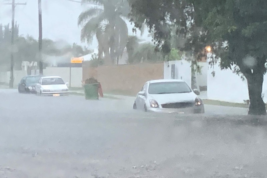 Cars parked on a street sit in flood waters