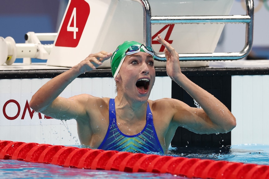 A woman screams with joy while in a pool wearing a green swimming cap 