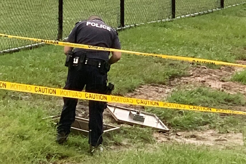 A police investigator photographs the site from behind yellow caution tape.