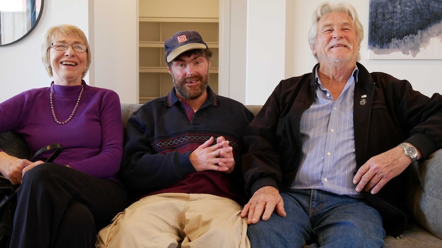 A woman and two men sit on a couch.