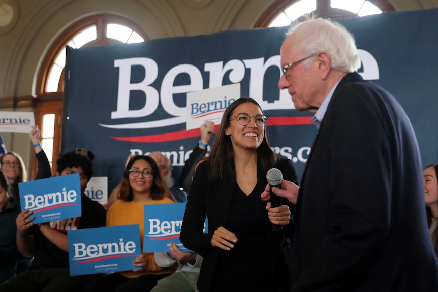 Alexandria Ocasio-Cortez and Bernie Sanders smiling at each other