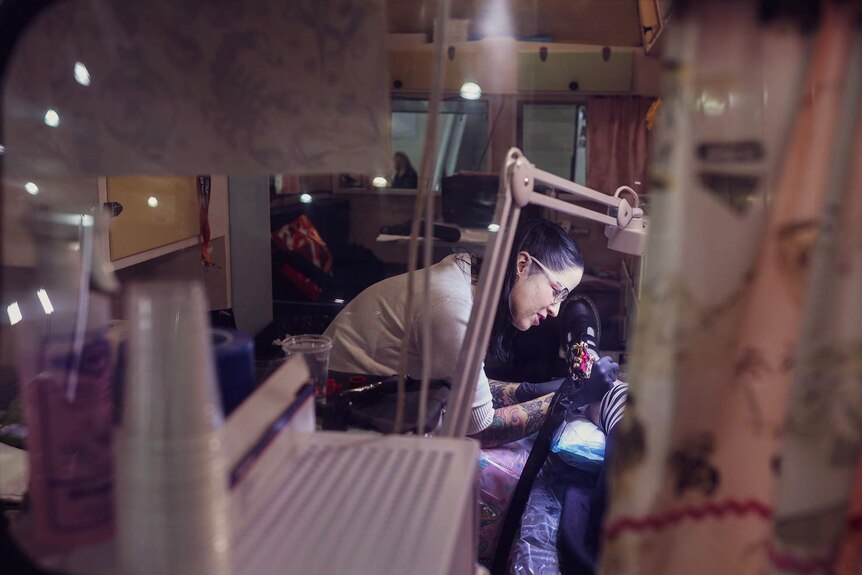 A Brisbane tattoo artist, Mimsy Gleeson, tattoos a woman's leg in her trailer trash studio