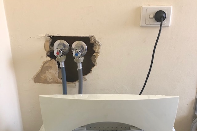 Gaping holes in a wall where washing machine pipes are plugged into a wall.