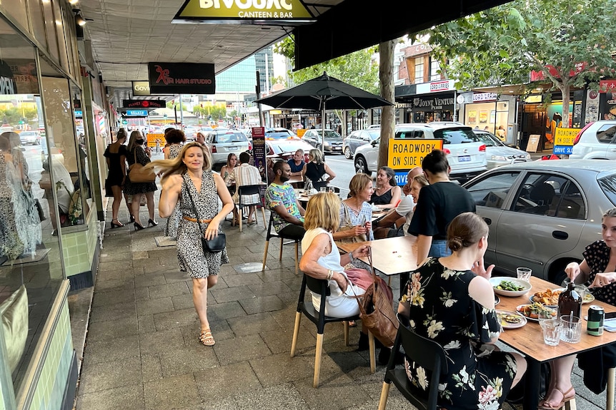A woman walks past tables on the sidewalk with people eating.