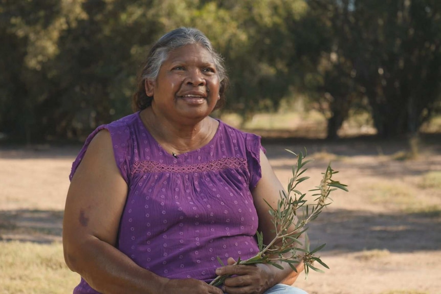Indigenous woman wearing purple holding a plant