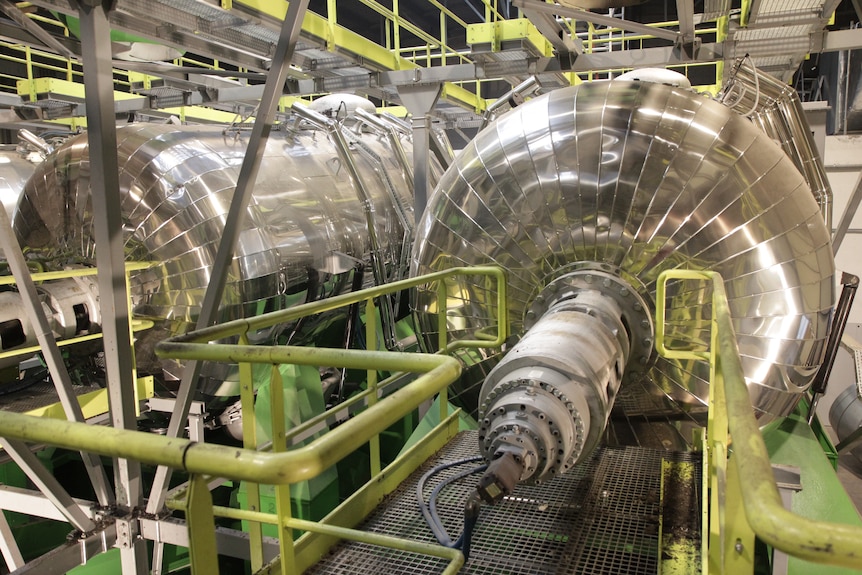 Machinery in a factory including two large silver vat-like parts.