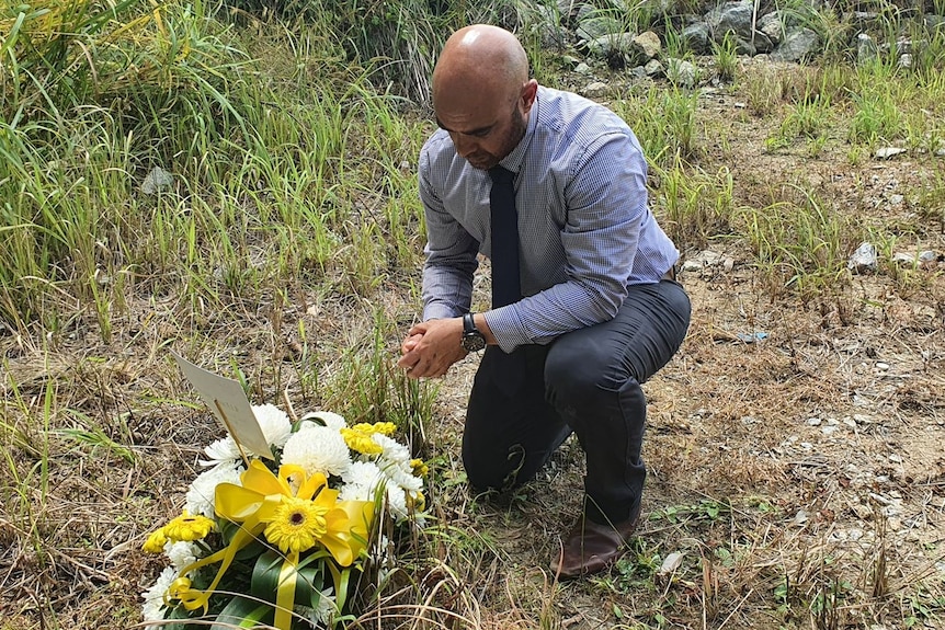 Man in formal attire kneeling down in a field with flowers on the ground.