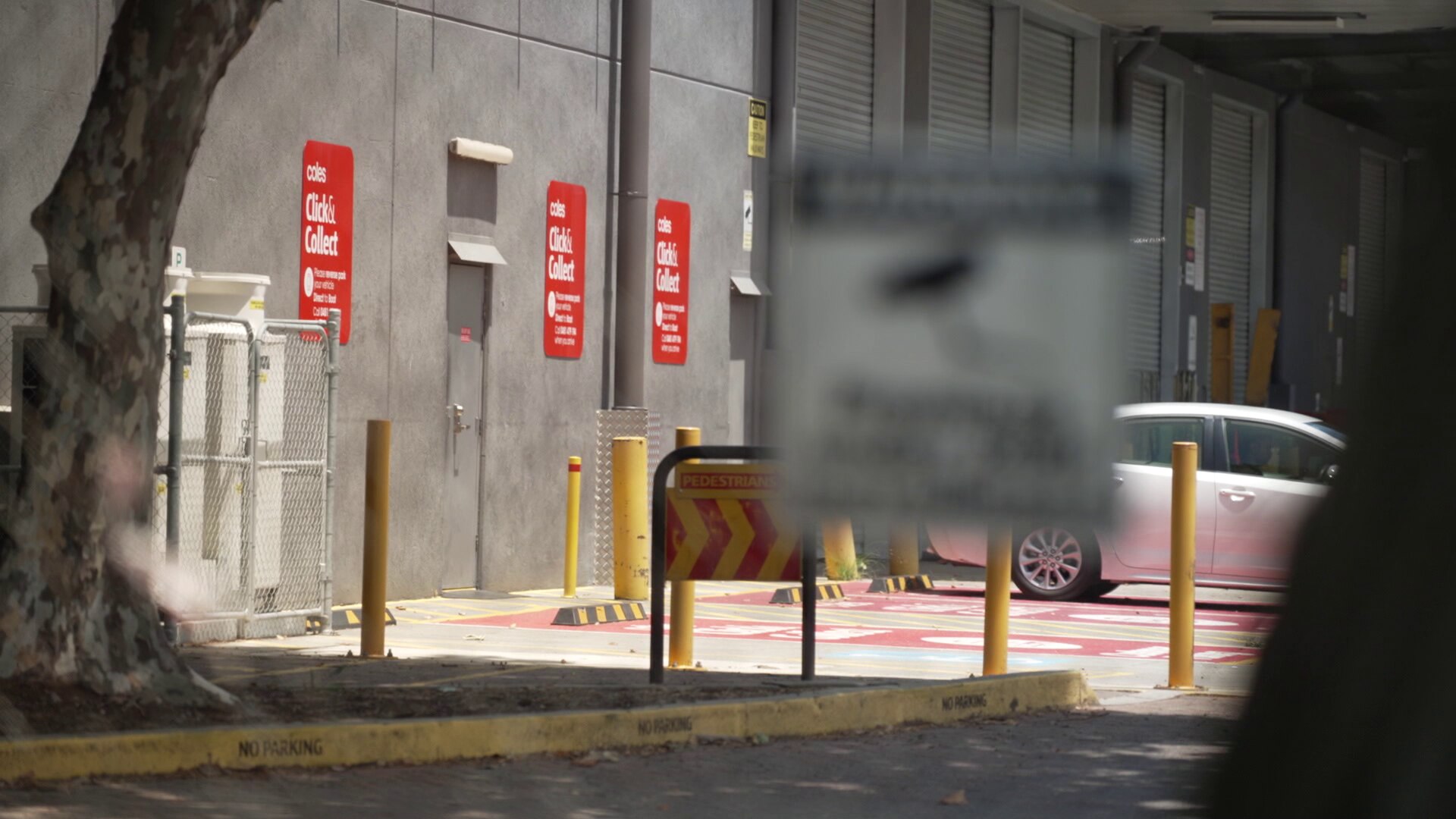 The click and collect parking area outside a Coles 'dark store', seen through a fence.