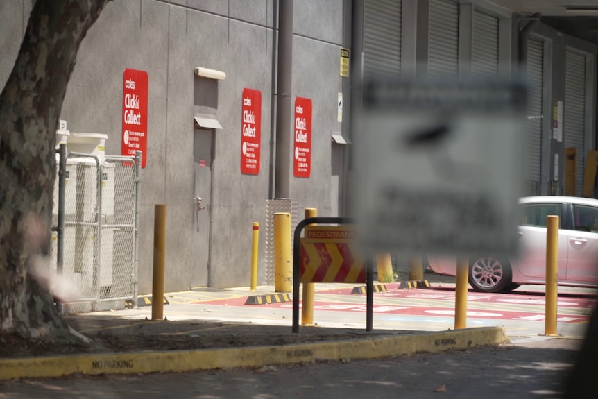 The click and collect parking area outside a Coles 'dark store', seen through a fence.