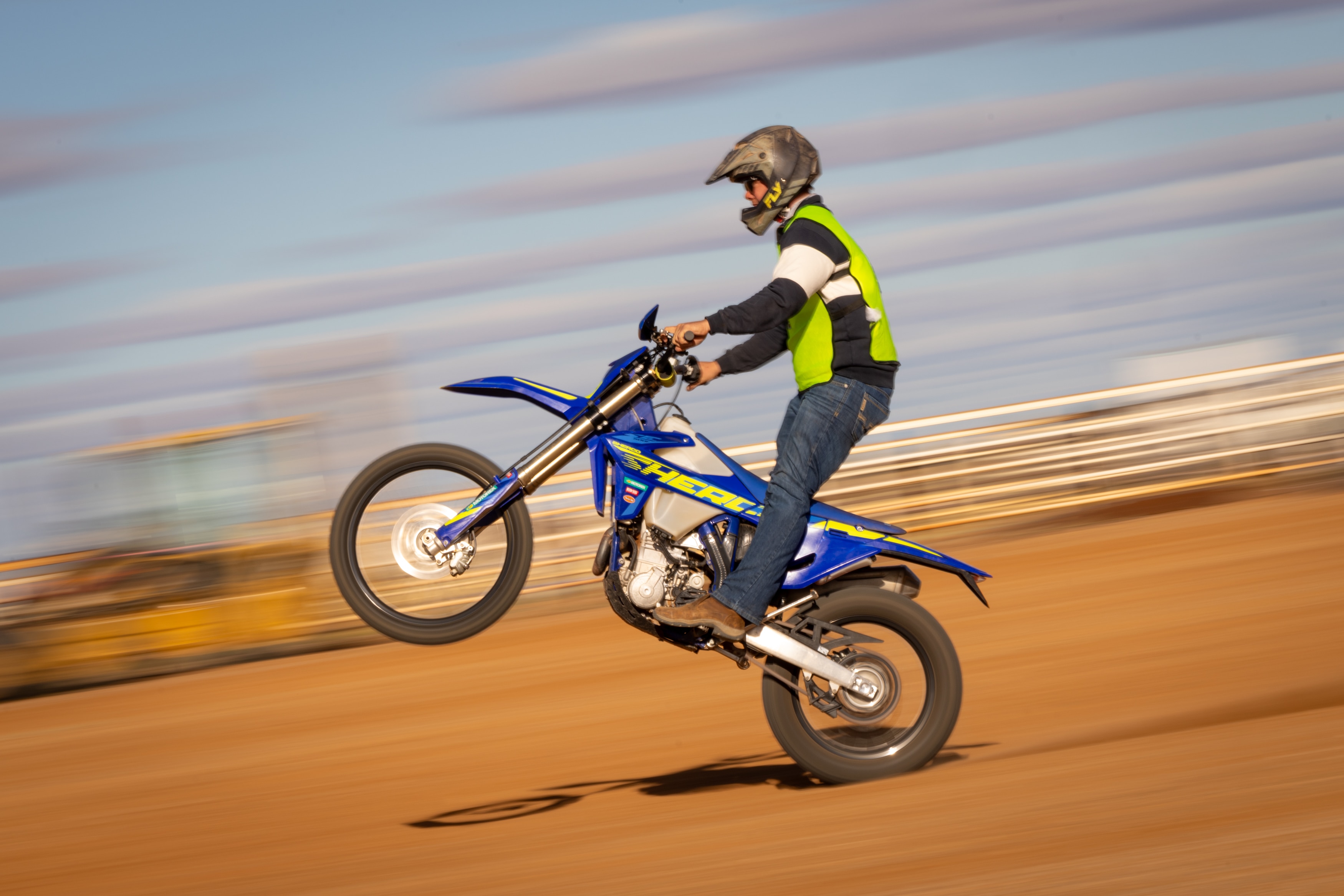 A man on a dirt track doing a wheelie on a motorbike