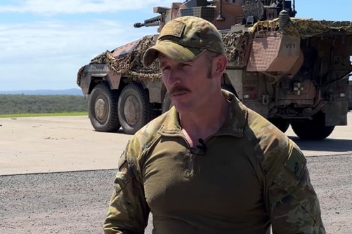 Soldier in uniform with boxer vehicle behind him