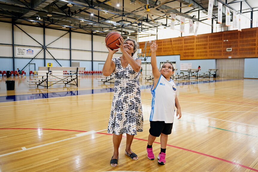 A young girl and her grandma play basketball. The girl is only young and is dressed in basketball clothes.