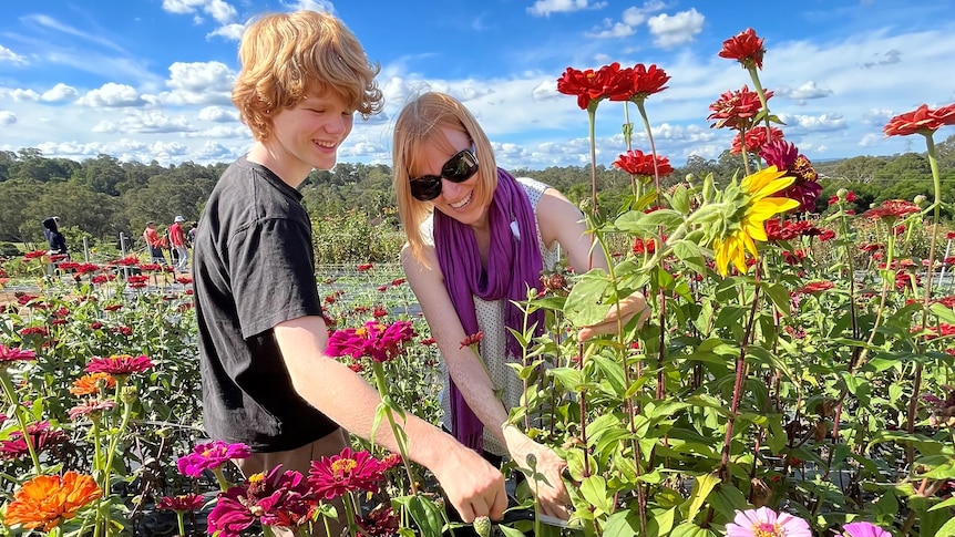A photo of a middle-aged woman in a field of flowers, standing next to her teenage son.