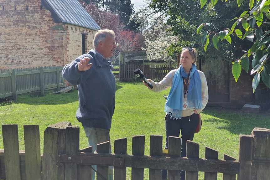 A woman holds a microphone out to an older man who is talking and gesturing. 