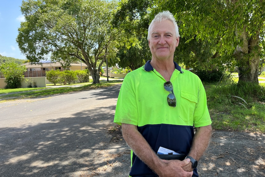 Man with grey hair in a green hi-vis shirt stands on driveway with a small smile on his face.