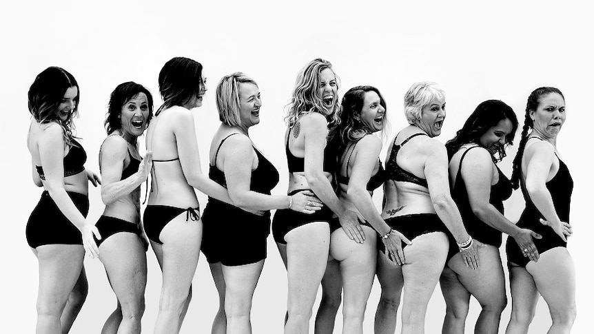 A group of nine women stand in their underwear.