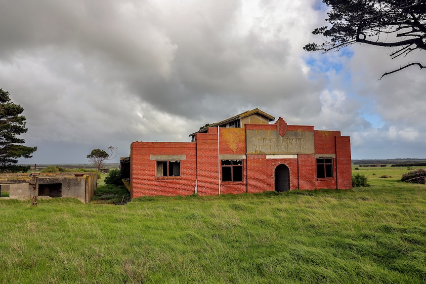 A tired brick building fallen to disrepair in a paddock beneath cloudy skies