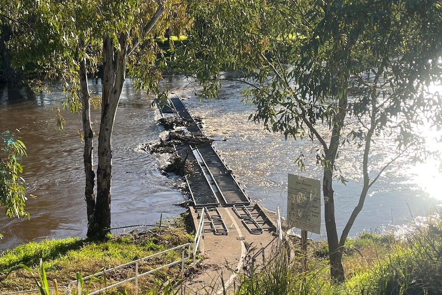 The top railings of a bridge can be seen through floodwater with pooled debris