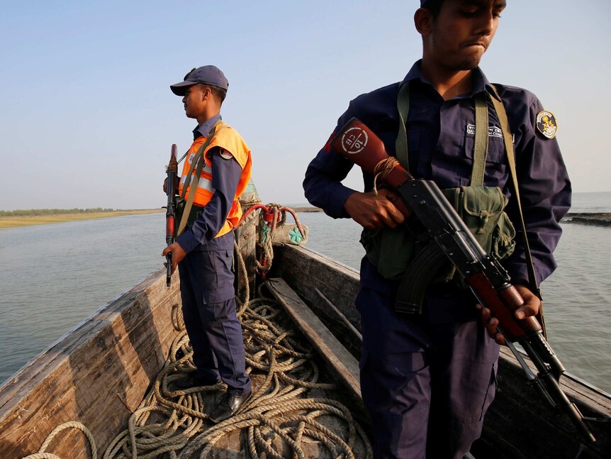 Two Bangladeshi men in uniform with big guns on an old fishing boat