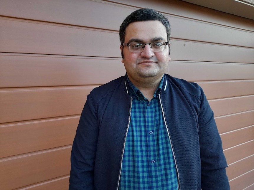 A man wearing glasses stands in front of a garage door.