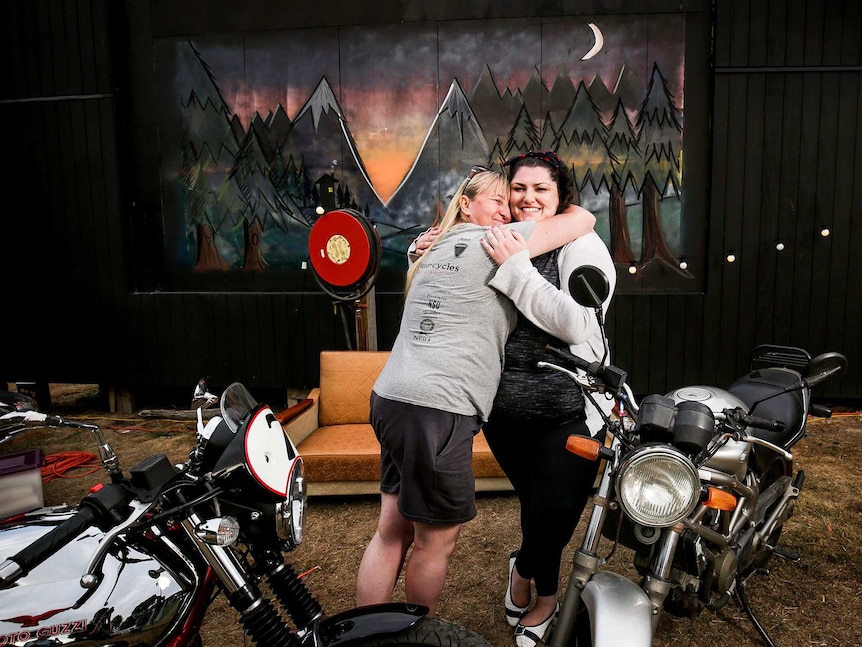 Tracy hugs Cassie, behind their bikes