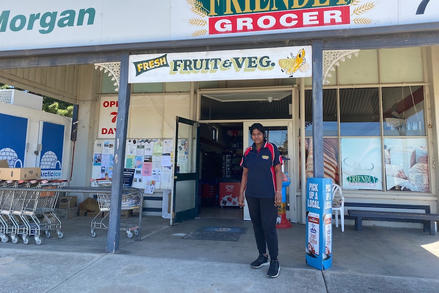 A woman standing in front of a store with a fruit and veg sign above