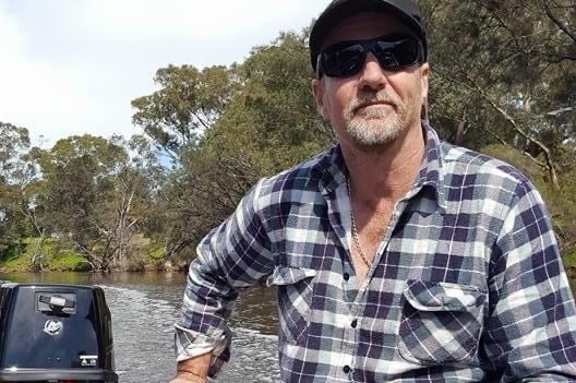 David Best wearing a checked shirt steering a boat in a river.