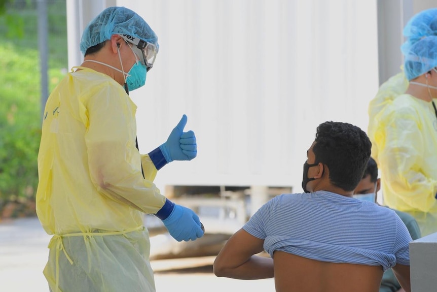 A health worker in PPE gives a thumbs up to a man in a face mask