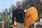 Surfer Luka Carstens-Hey stands on the sand in his rashie and boardshorts with his surfboard on the walkway to Burleigh Beach.