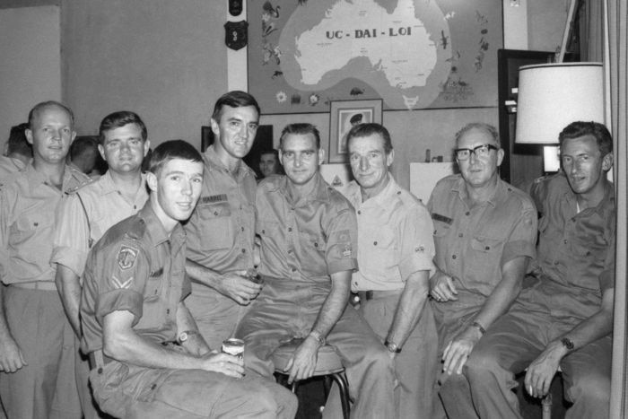 Black-and-white photo of eight relaxed Australian soldiers inside a mess hall, some standing while other hold cans of beer