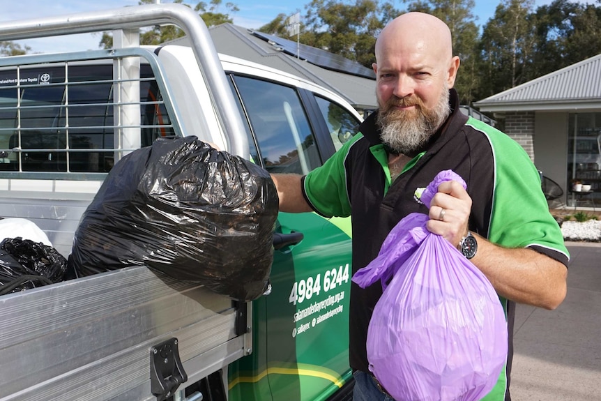 man putting two garbage bags filled with foil into the back of his ute