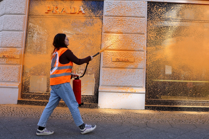 A woman sprays the outside of a Prada store in bright orange paint.