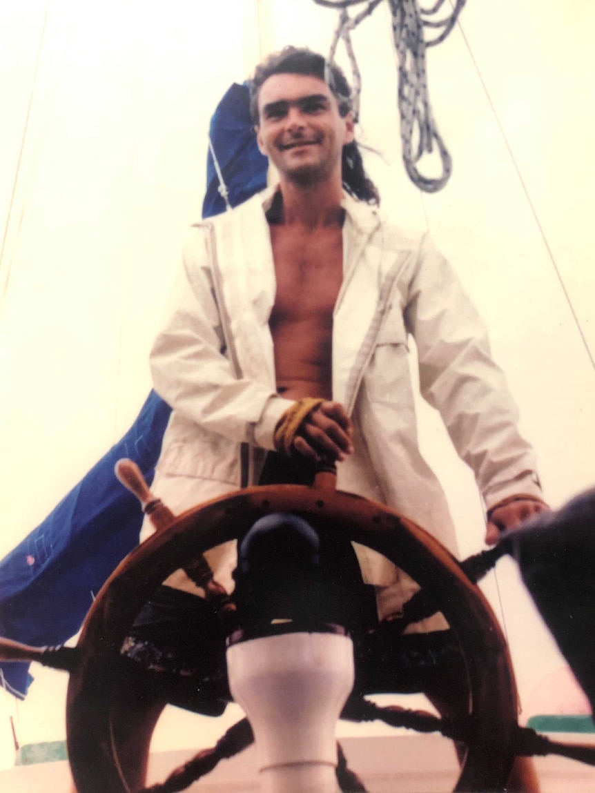 Young man stands at the helm of a ship in old photo.