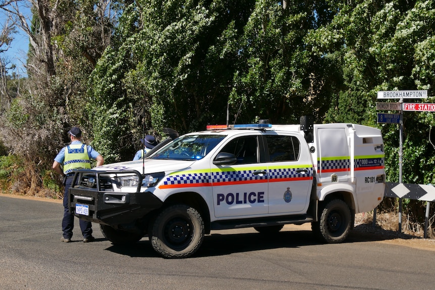 A police vehicle with two officers standing outside parked on a country road. 