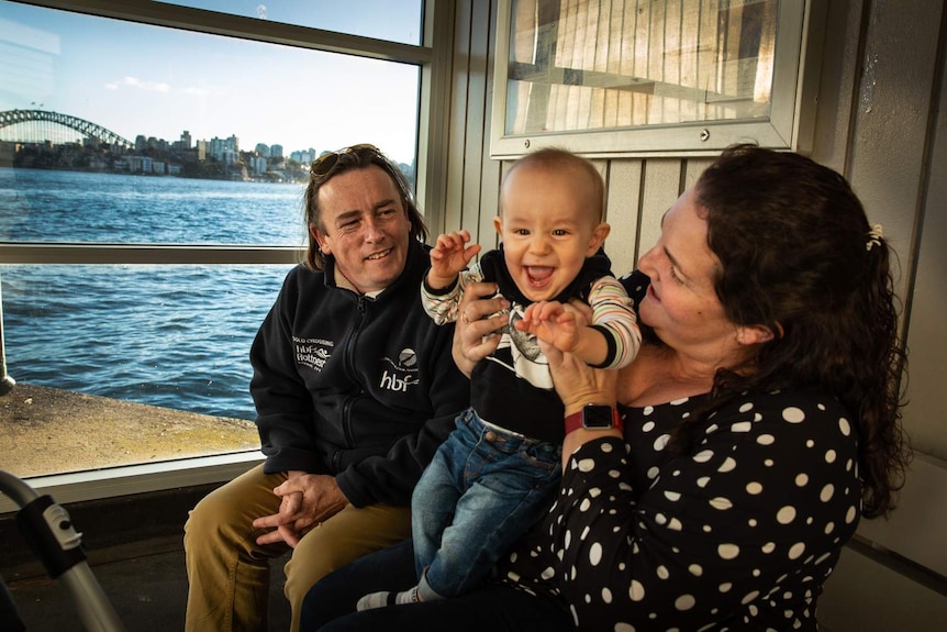 A couple with a young baby in sitting in a wharf on the edge of the harbour.