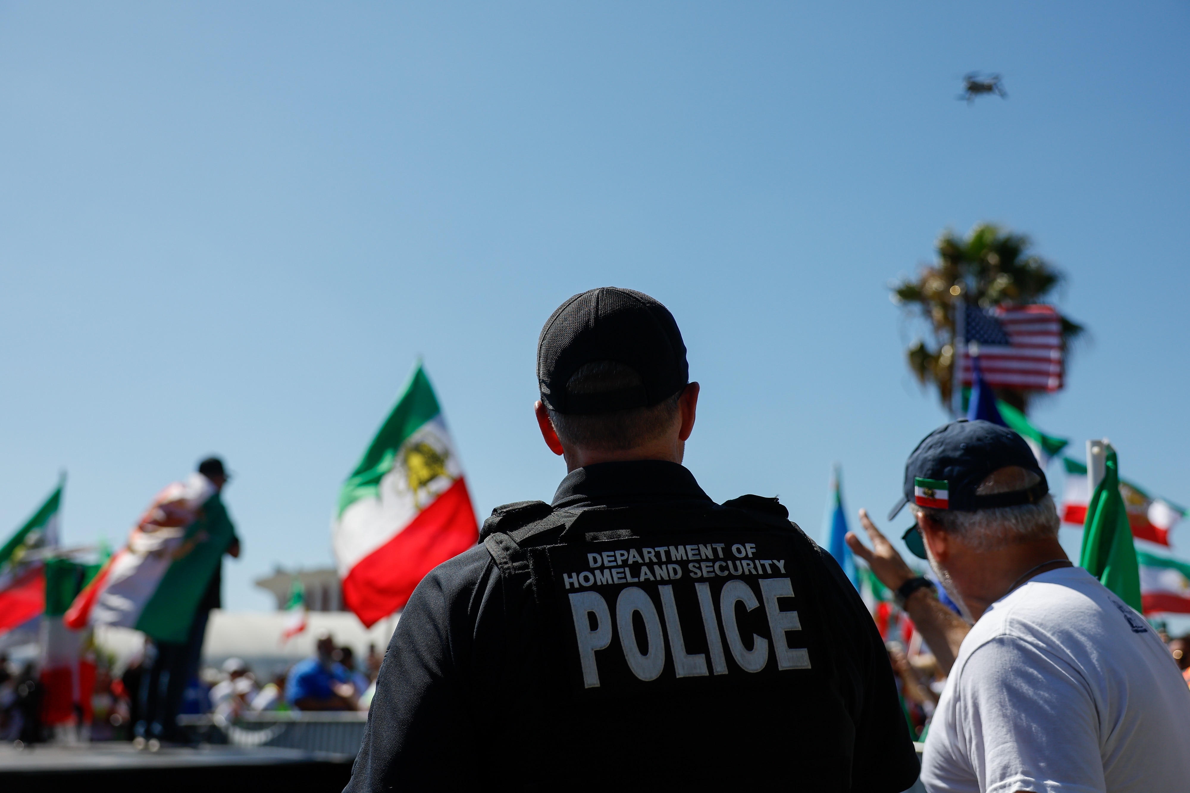 A police officer watches a drone flying through the air, Iran flags flying.