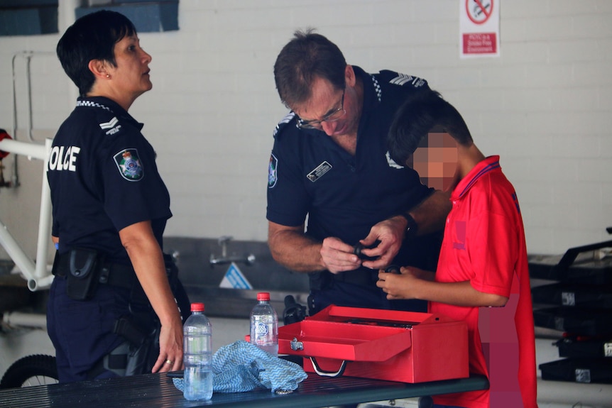 Two police officers work with a boy on bike repairs