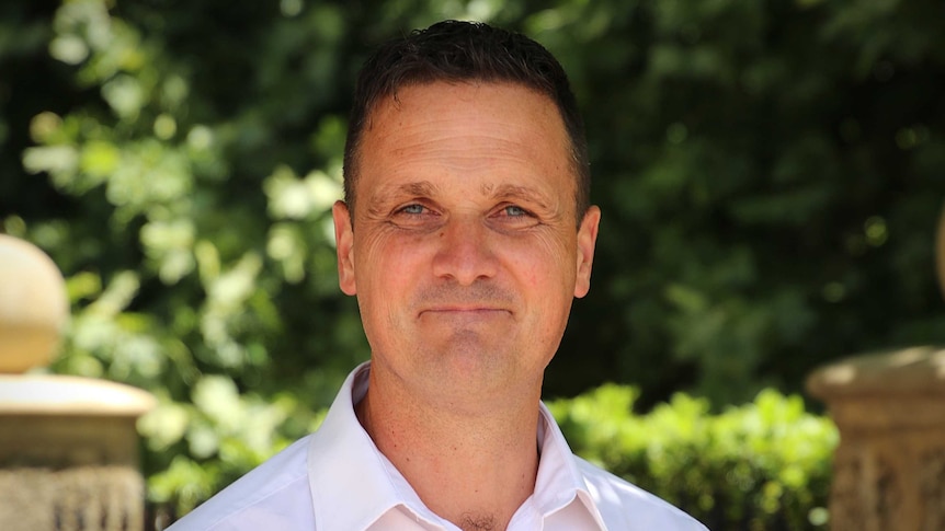 A man wearing a collared shirt smiles and poses for a photo