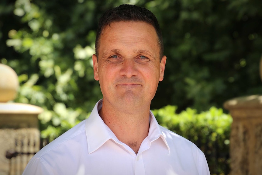 A man wearing a collared shirt smiles and poses for a photo