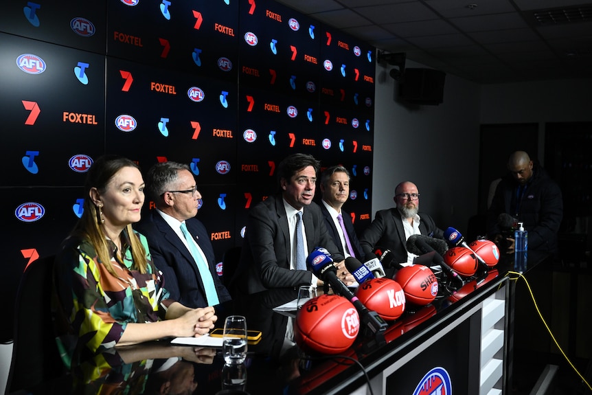 Gillon McLachlan is among a number of people sitting at a desk during a press conference