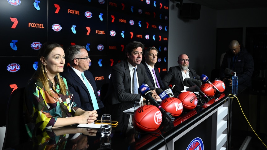 Gillon McLachlan is among a number of people sitting at a desk during a press conference