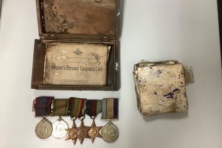 Old rusted and dirty war medals, documents, and faded photographs flat laid on a white table 