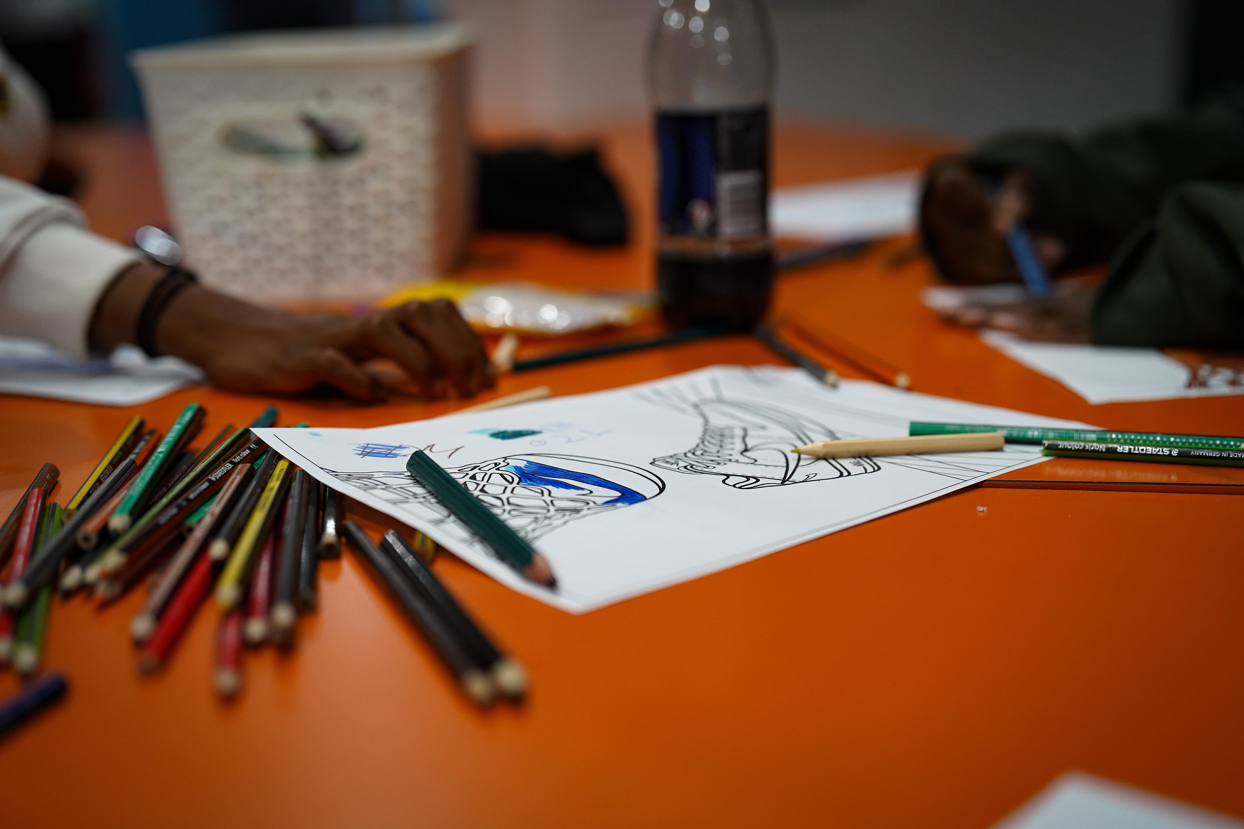 Coloured pencils on a desk next to a drawing of shoes.