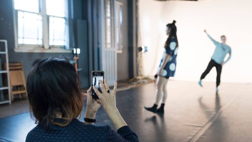 A woman uses a smartphone to capture a gif of two dancers in motion.