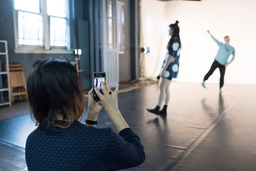 A woman uses a smartphone to capture a gif of two dancers in motion.