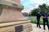 Two police officers walk next to a vandalised statue